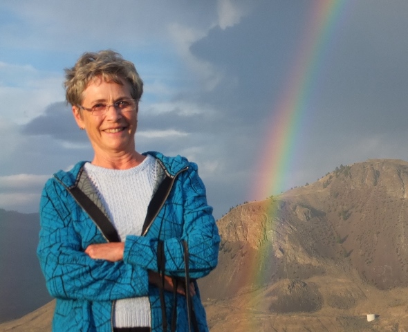 Woman standing on top of mountain with rainbow in background